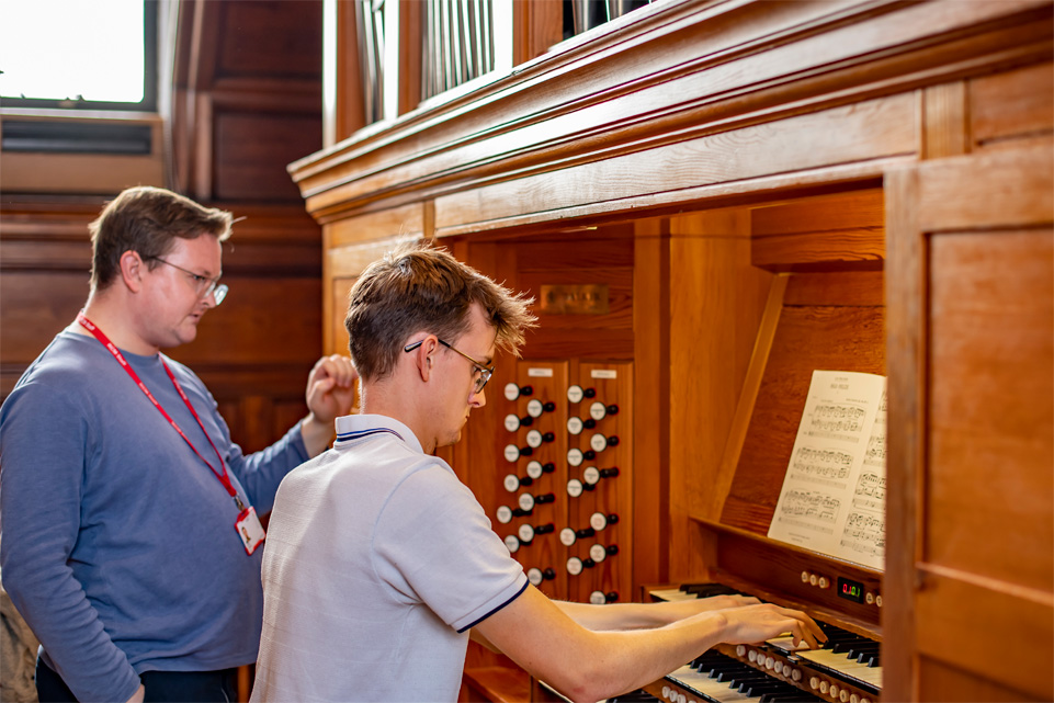 Student practising on the organ in the West Parry Room, with a man teaching the student.